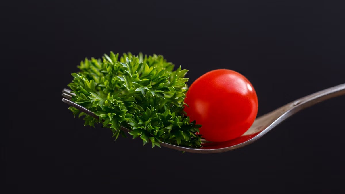 Close-up of a cherry tomato and parsley on a fork against a dark background.